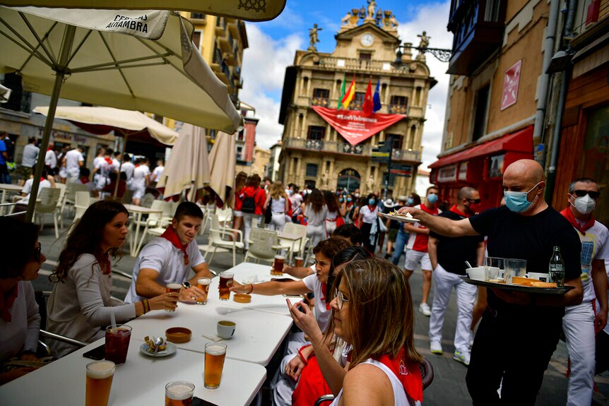 Residents, wearing white clothes and traditional red scarves, enjoy lunch outside the City Hall in Spain.