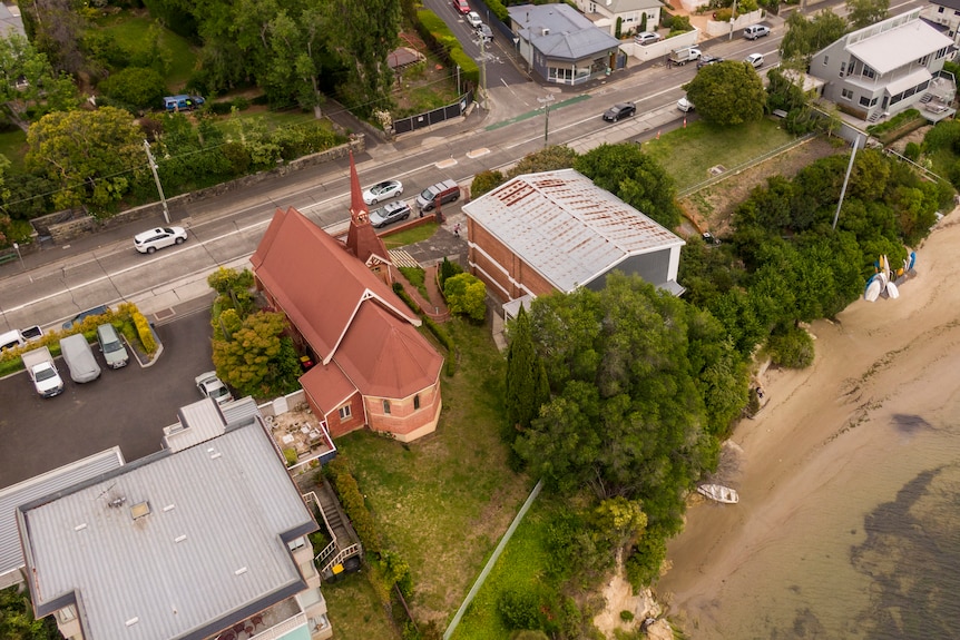 An aerial view of a church and church hall by the water's edge.