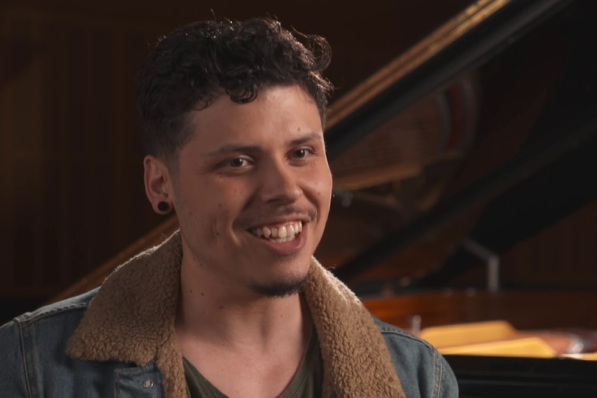 Man in front of a piano speaking to an interviewer.