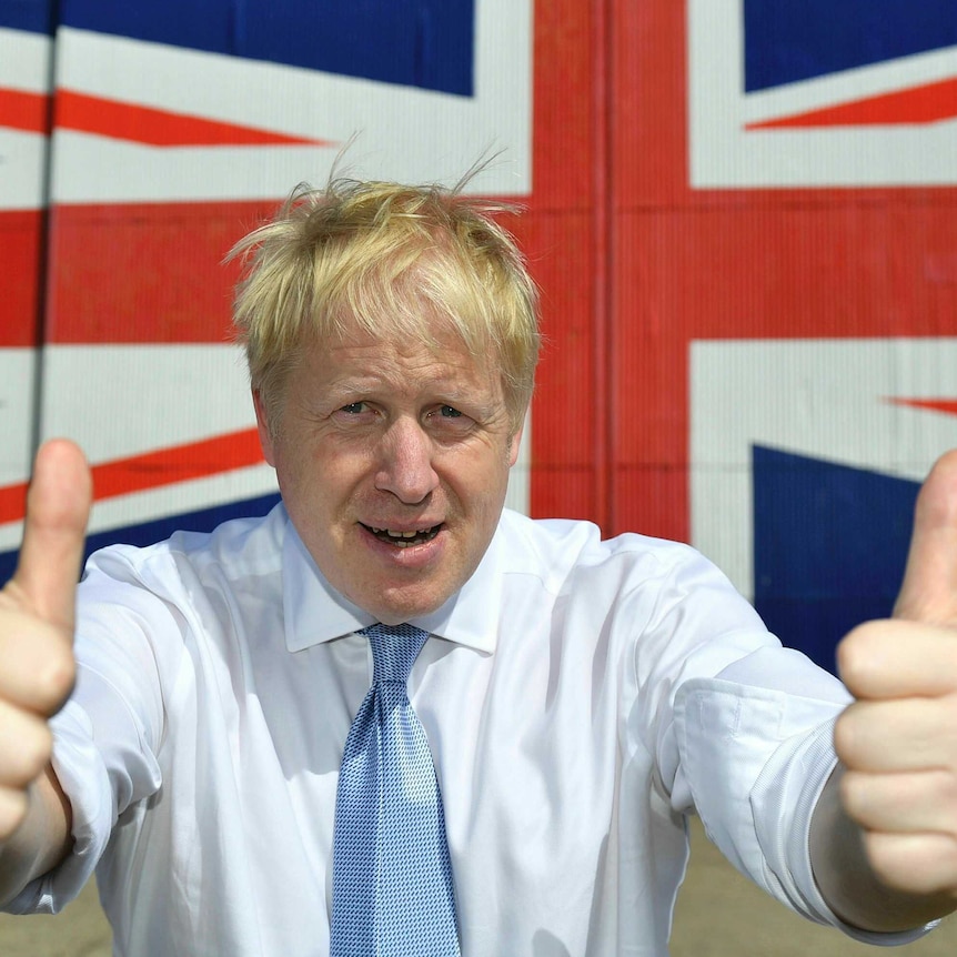 A man with blond hair gives a thumbs up to the camera