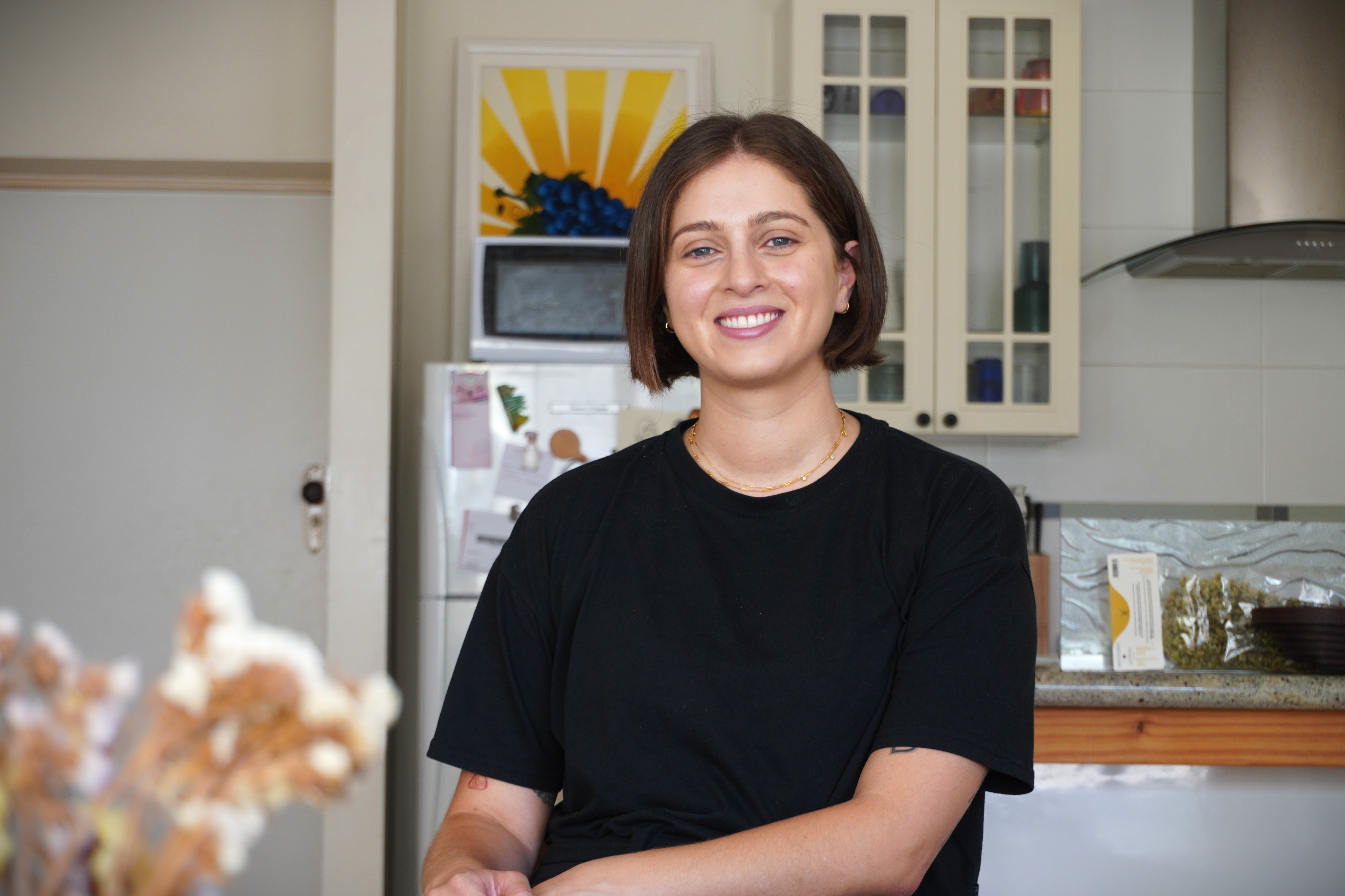 Woman with brown short hair sits in her kitchen wearing a black T-shirt.