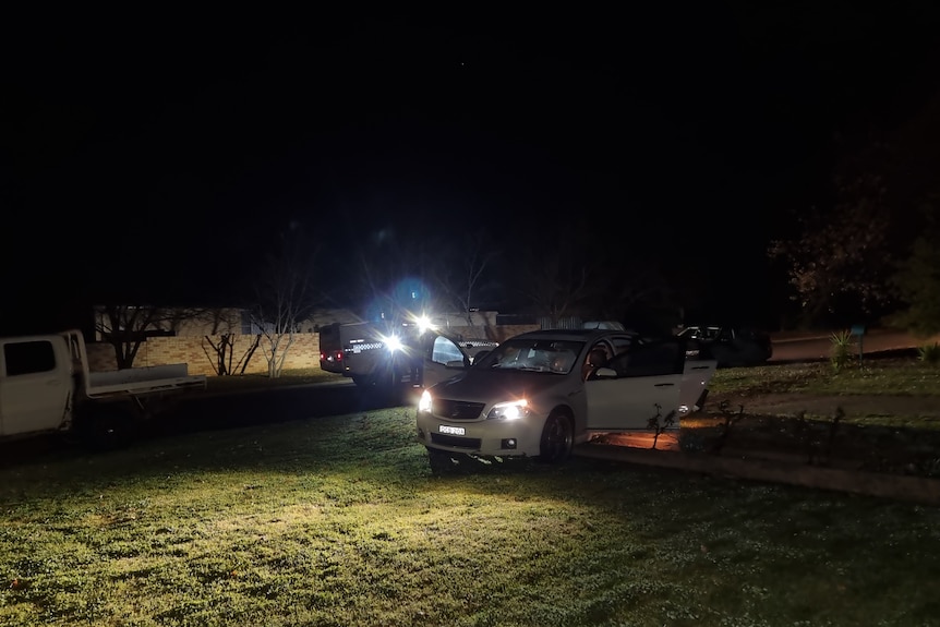 A sedan with its lights on parked in a field at night.