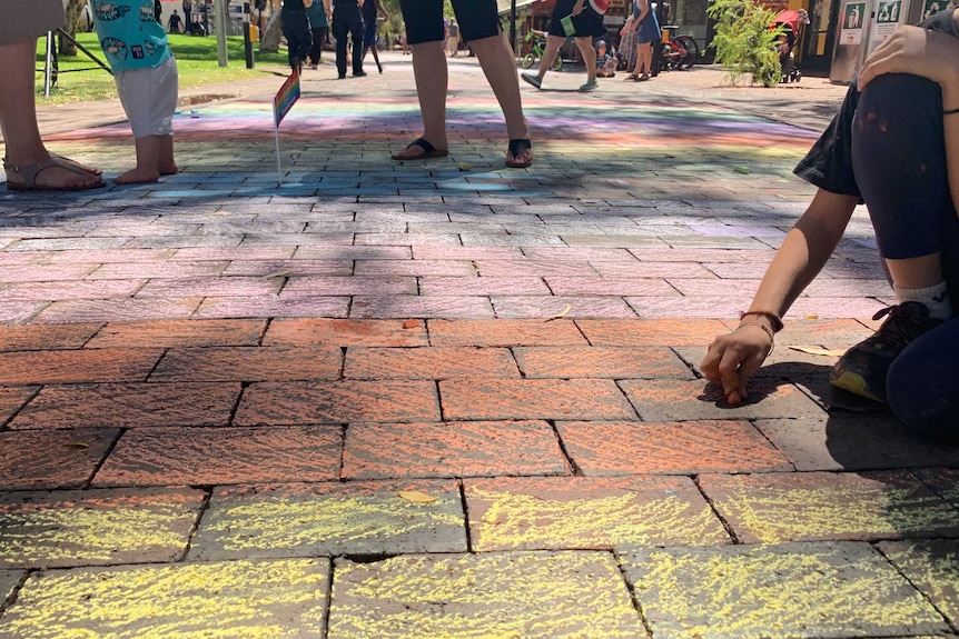 Un centro comercial de ladrillos coloreado con tiza en los colores del arco iris con gente caminando en el centro comercial.