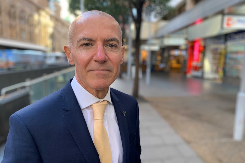 Silvio Del Vecchio stands on a street wearing a blue suit and pale yellow tie