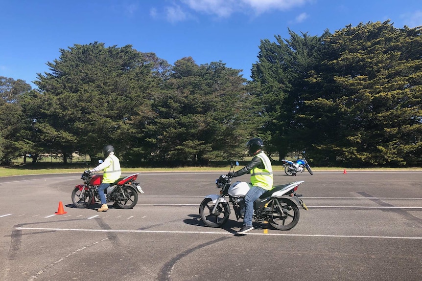 Two motorcyclists in hi-vis vests prepare to ride around a training course.