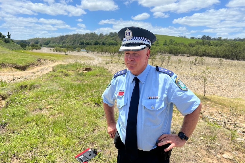 A uniformed police officer stands in a hilly paddock.