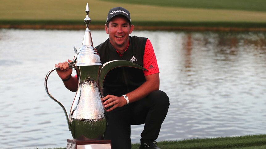 Lucas Herbert crouches down next to a massive silver trophy shaped like an ornate tea pot