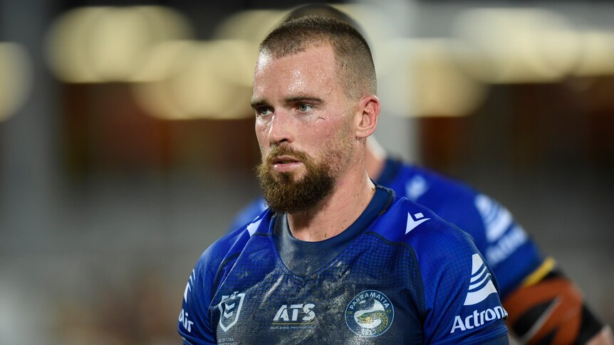A tired NRL player, with mud on his shirt, looking disappointed at a defeat