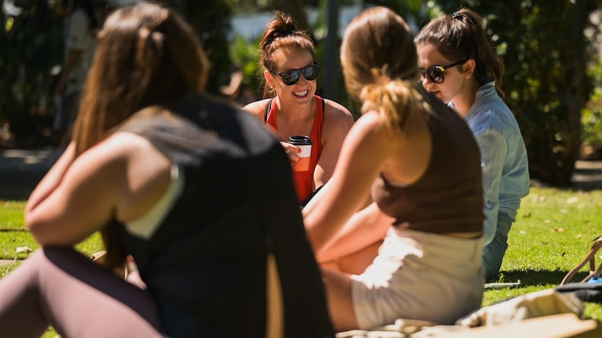 People sitting on the grass in the sun drinking coffee and laughing