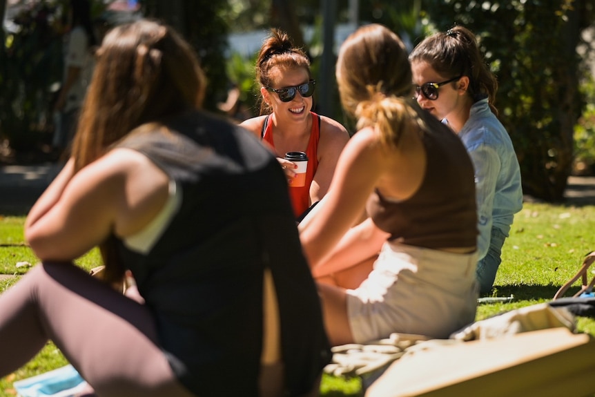 People sitting on the grass in the sun drinking coffee and laughing