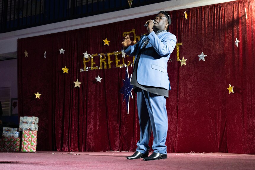 Bishop Lawrence Rolle on stage wearing a dark blue suit and holding a microphone. 
