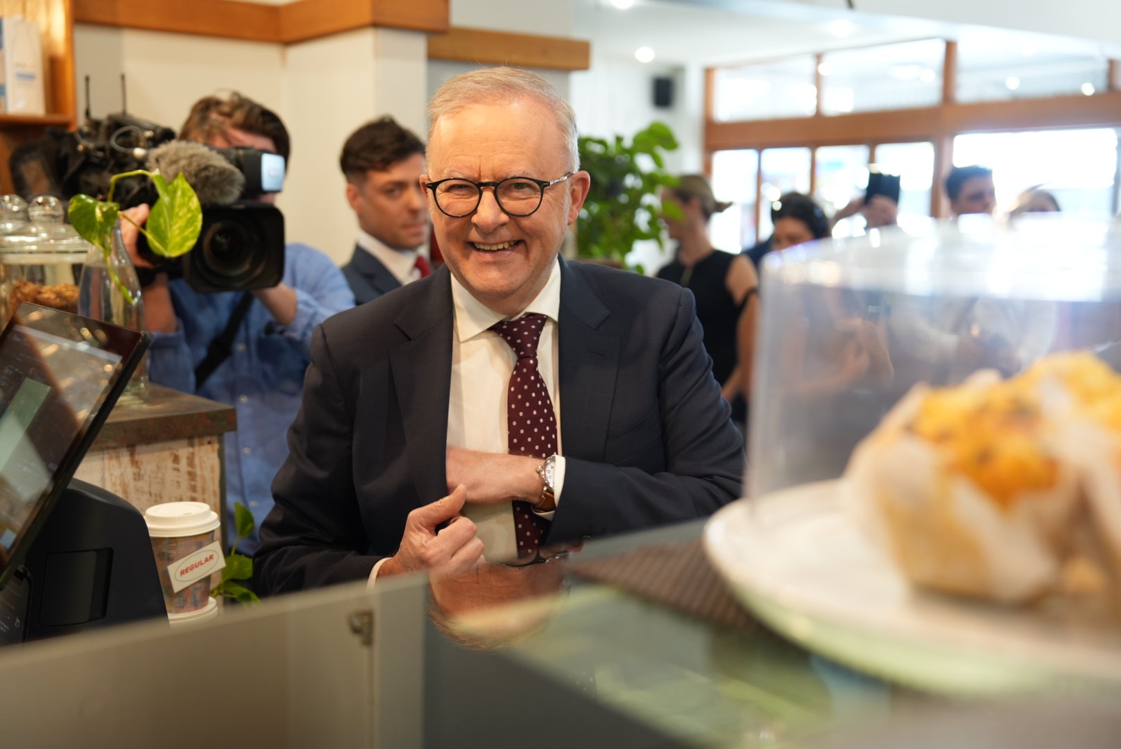 Anthony Albanese smiling as he is pictured next to muffins in a cafe
