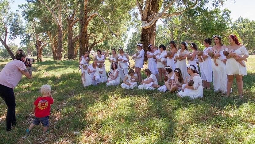 A photographer takes a photo of women breastfeeding their babies with other children nearby