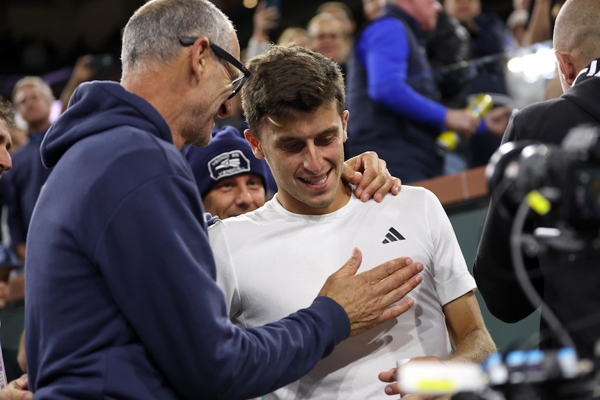 A tennis coach puts his arm around a smiling player after his win over Novak Djokovic.
