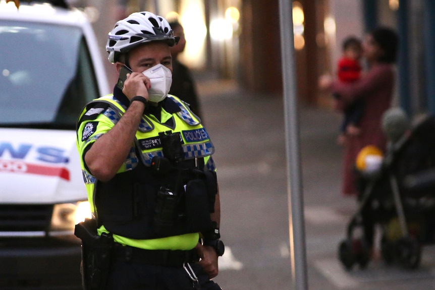 A police officer wearing a mask and helmet talks on a mobile in front of a 9 news van on Murray St.