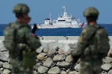 Two soldiers in camouflage look at a Philippine Coast Guard vessel sailing on open water 