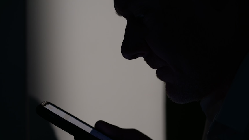 A man's side profile in shadows with a phone close to his face