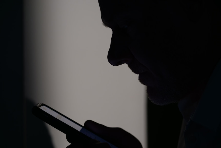 A man's side profile in shadows with a phone close to his face