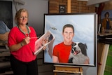 Kathie Bowtell stands next to a portrait on an easle.