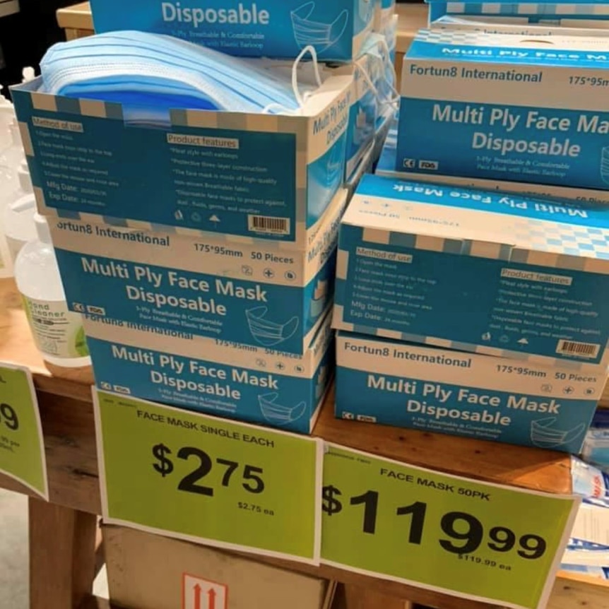 A $119.99 price tag in front of boxes of 50-pack face masks stacked on a supermarket shelf. 