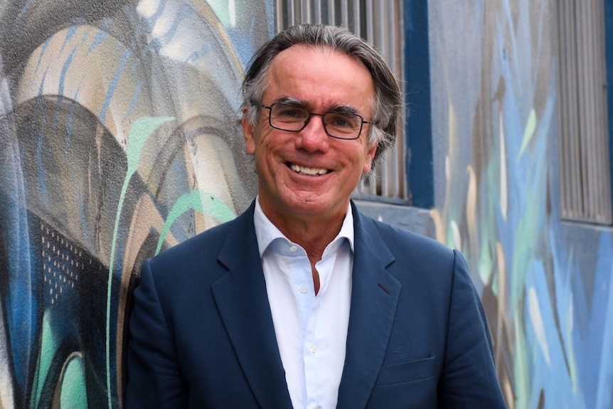 a man in a dark suit smiles beside a graffiti wall