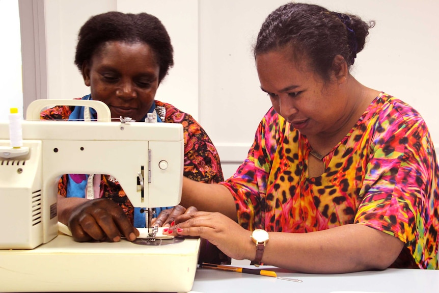 Two women work behind a sewing machine.