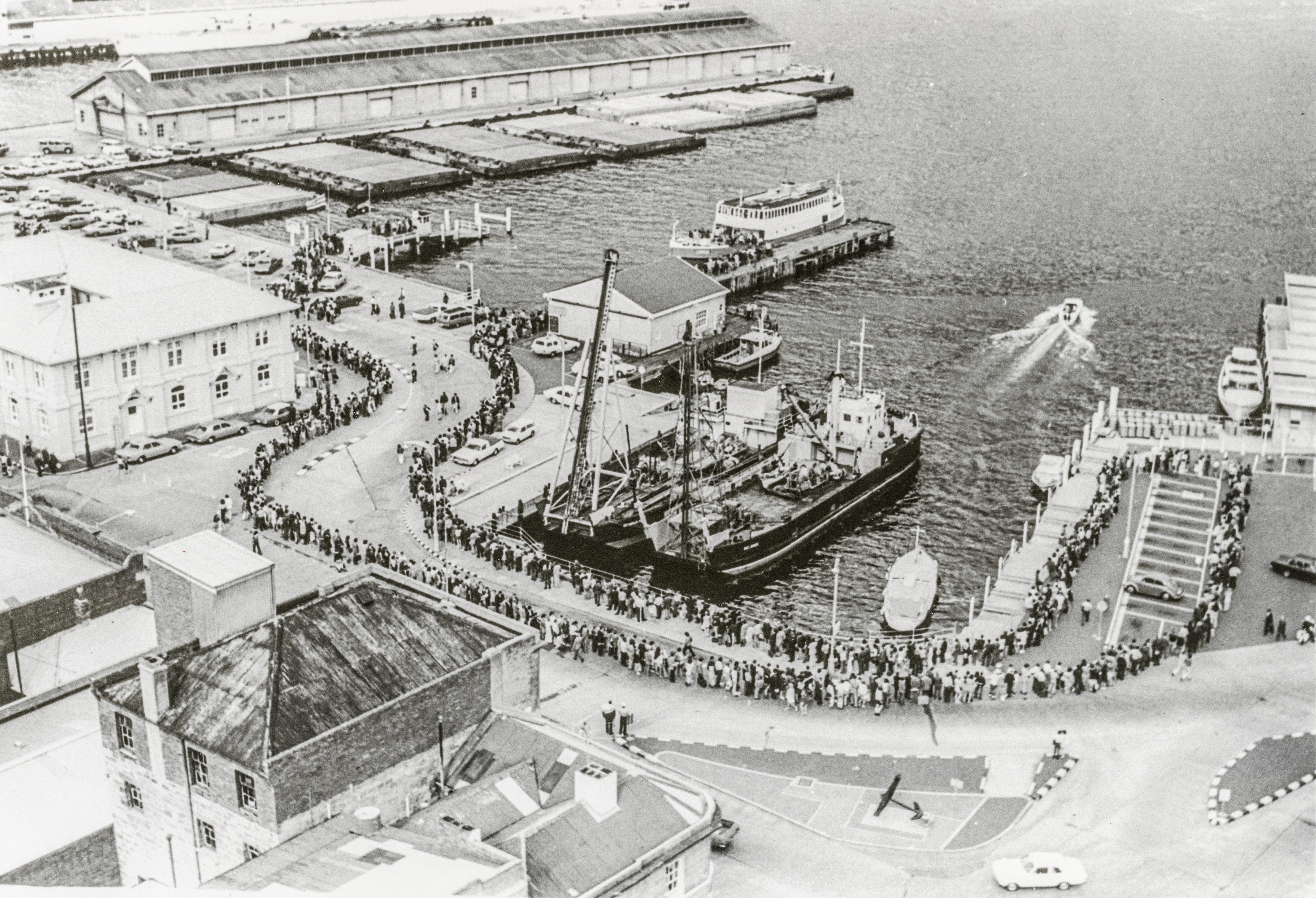 A queue of people snaking down several streets on Hobart's waterfront in an old black and white photo.