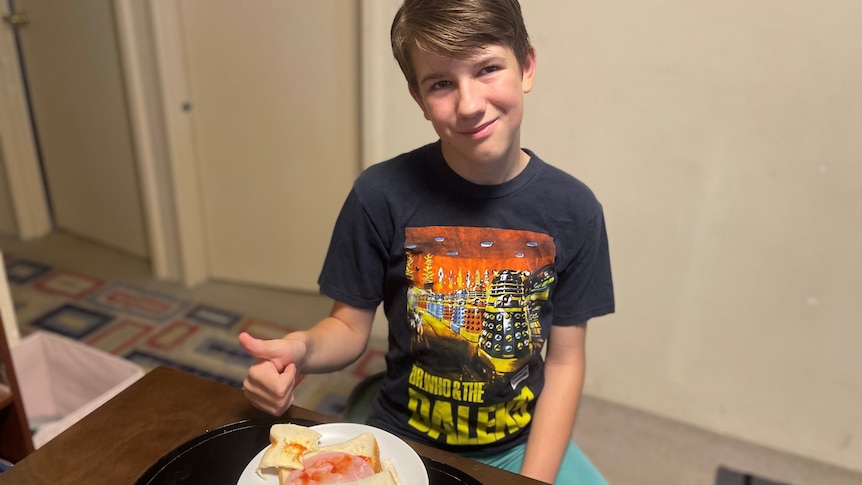 A young boy in a Dr Who t-shirt gives his ham sandwich the thumbs up. 