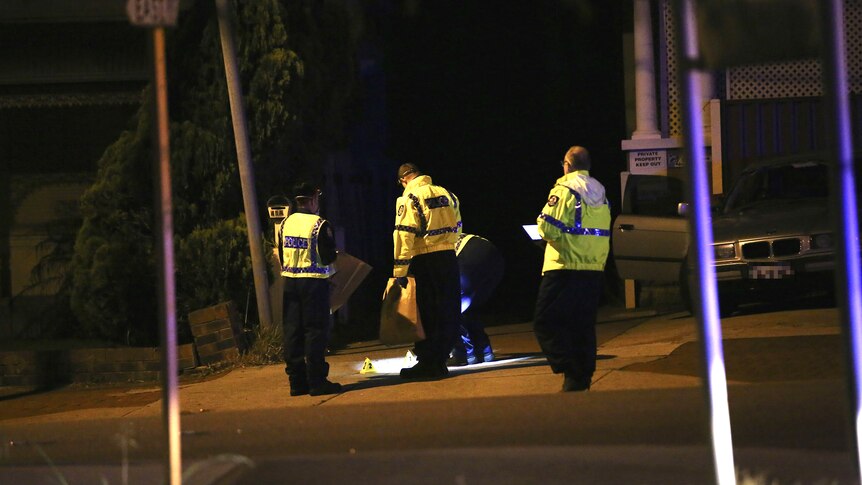 A wide shot showing four police officers in hi-vis clothing looking at something on the ground in a street.