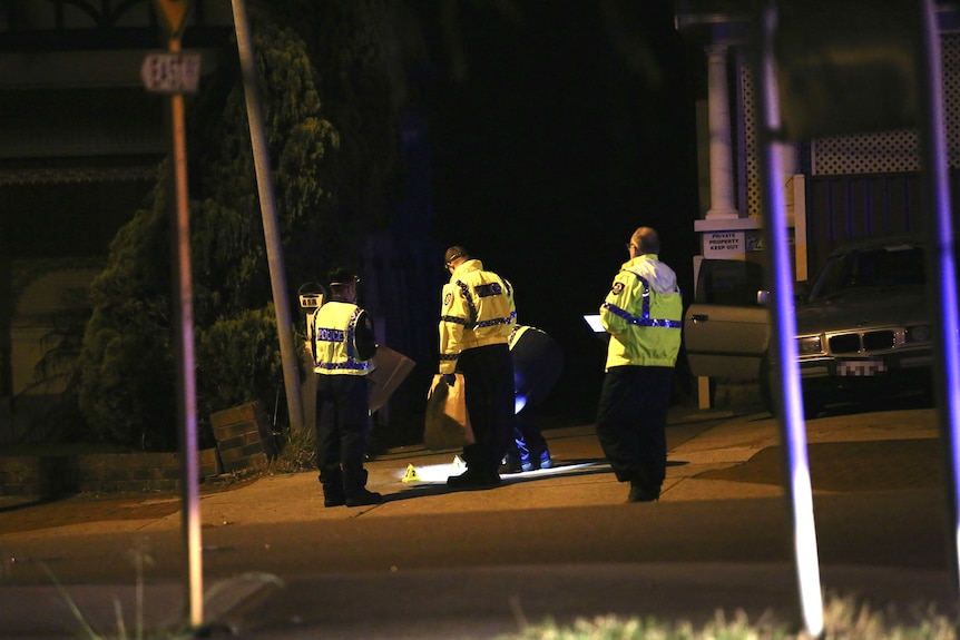 A wide shot showing four police officers in hi-vis clothing looking at something on the ground in a street.