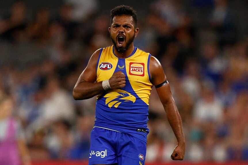 Willie Rioli stands with his mouth open and fist closed to thump his chest