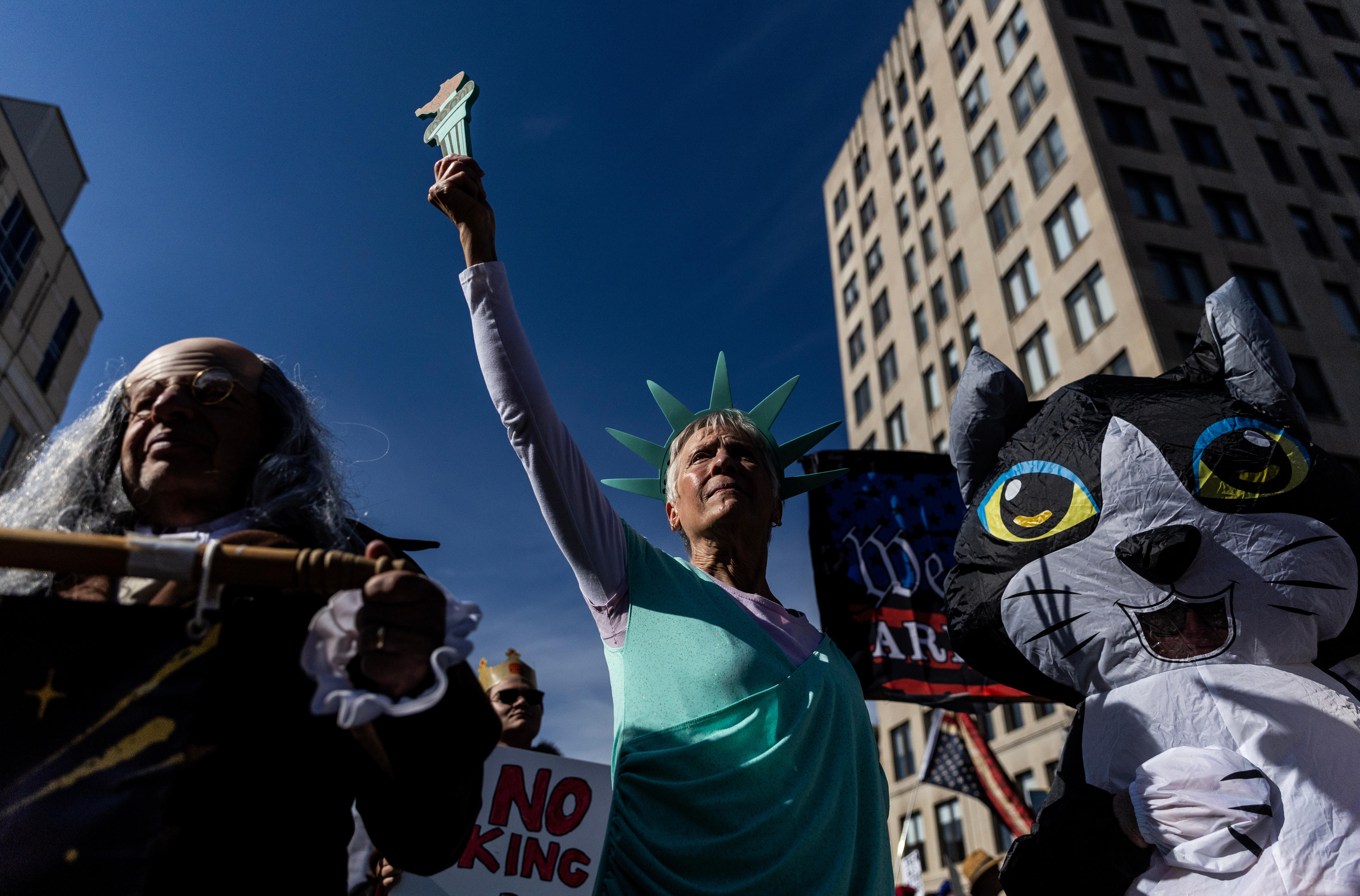 People dressed as Benjamin Franklin, the Statue of Liberty and a cat in front of protest signs
