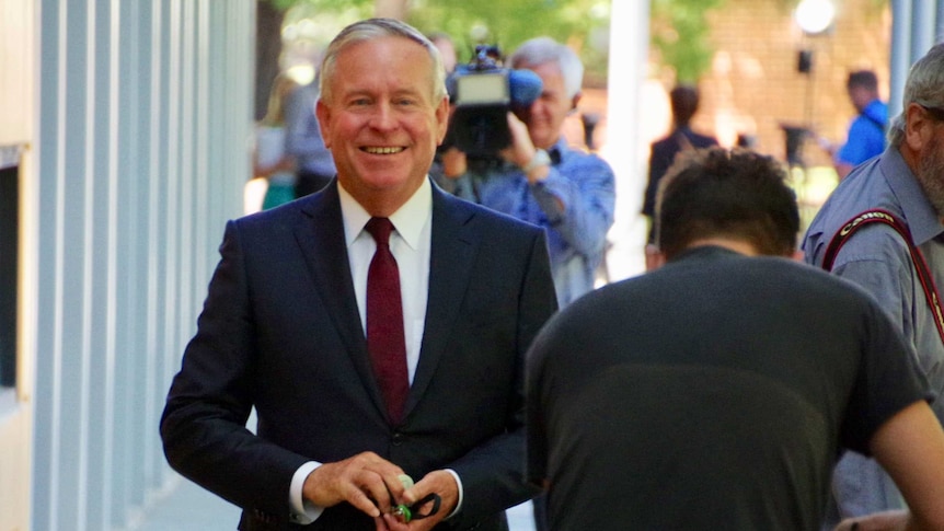 Former WA premier Colin Barnett walks outside the ABC buildings, surrounded by TV camera operators and photographers.