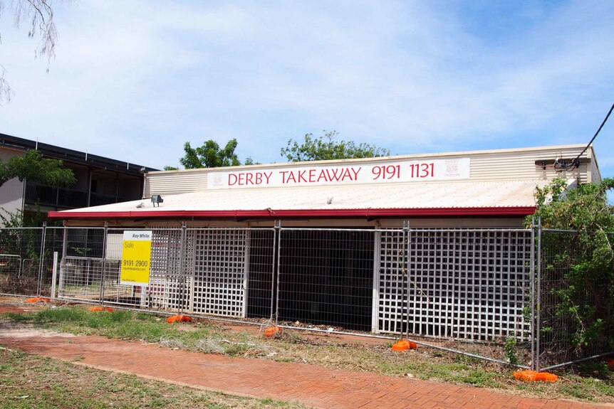 A derelict Derby takeaway restaurant sits fenced off with a real estate sign on the fence.