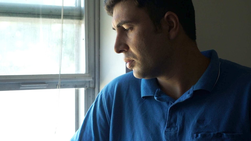 A close-up photo of a man in a blue shirt looking out a window.