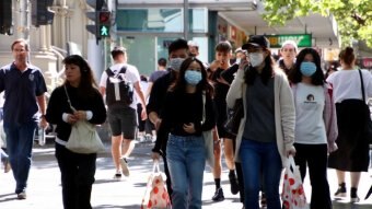 People walk down a busy CBD street with facemasks on.