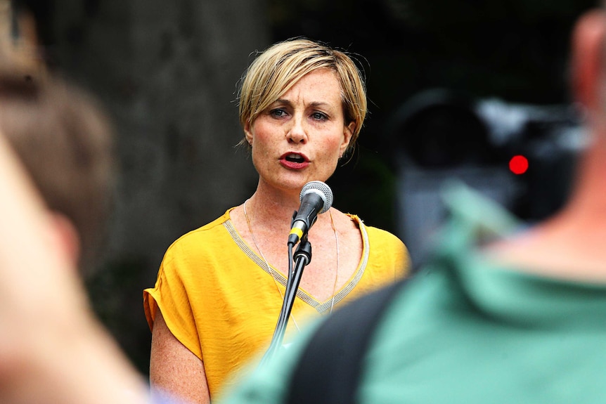 A mid shot of Sam Lee from Gun Control Australia speaking at a rally in Sydney while wearing a yellow top.