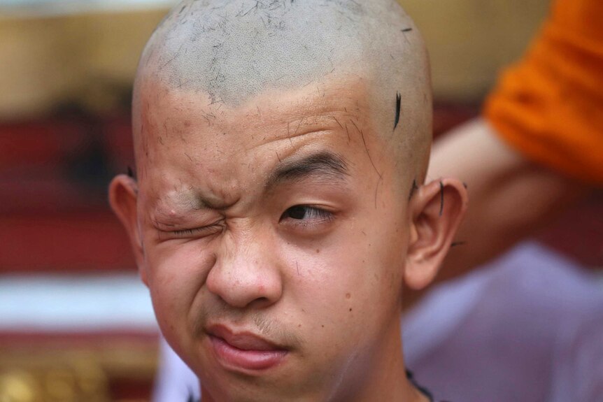 Team member Pornchai Kamluang pulls a face while getting his head shaved