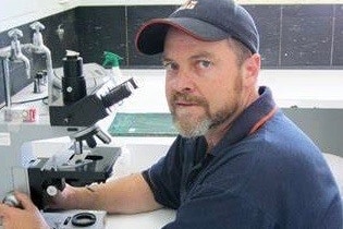 A man in a blue shirt sits in a lab.