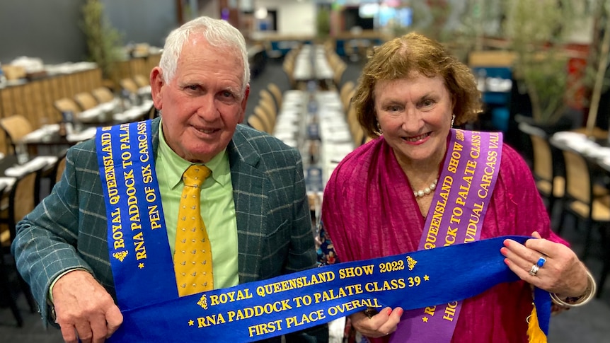A man and a woman stand in front of a table with show ribbons