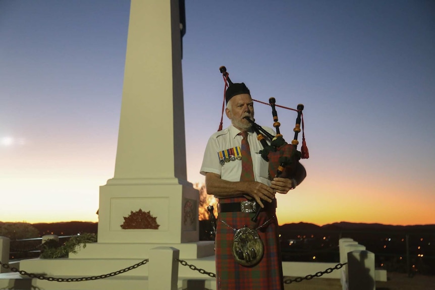 a man uniform with medals playing the bagpipes next to a monument as the sun rises