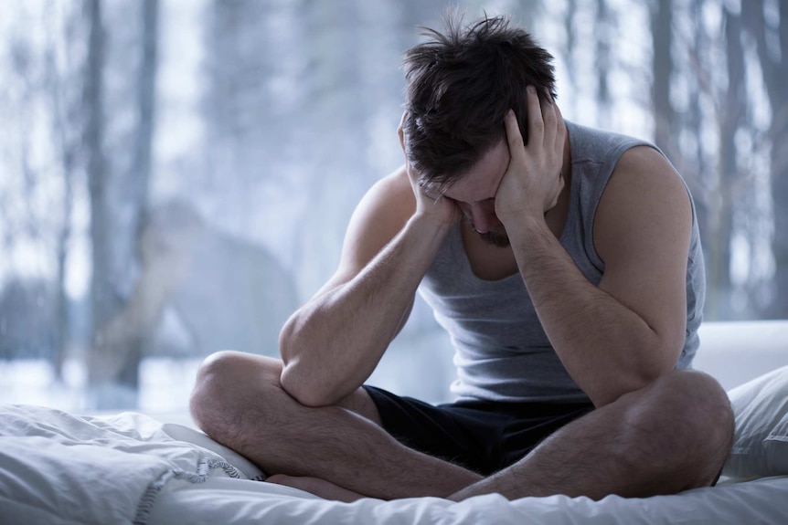 A man upset with his head in his hands sitting on a bed