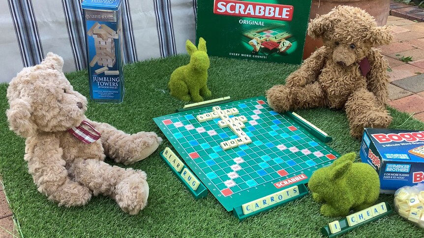 Two teddy bears sit in a driveway playing scrabble.