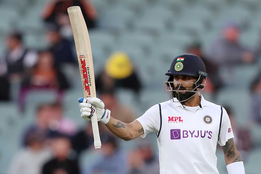 VIrat Kohli raises his bat vertically in the air wearing a batting helmet.