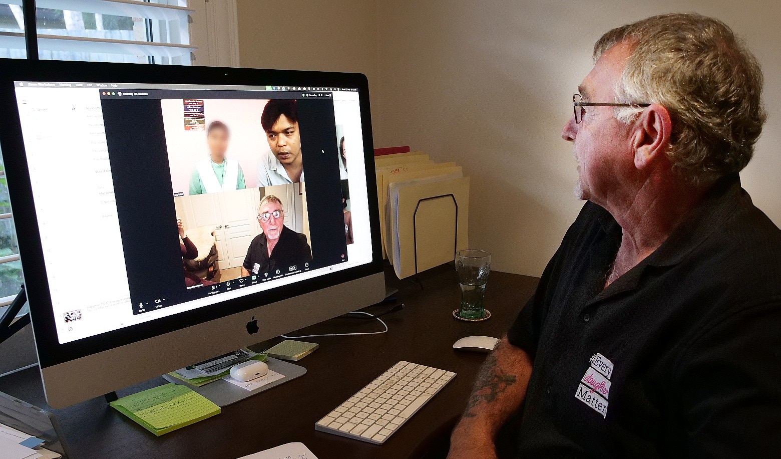 Na tela aparece um homem em videochamada com parceiros nepaleses: a mulher com uniforme azul-marinho e rosto desfocado.