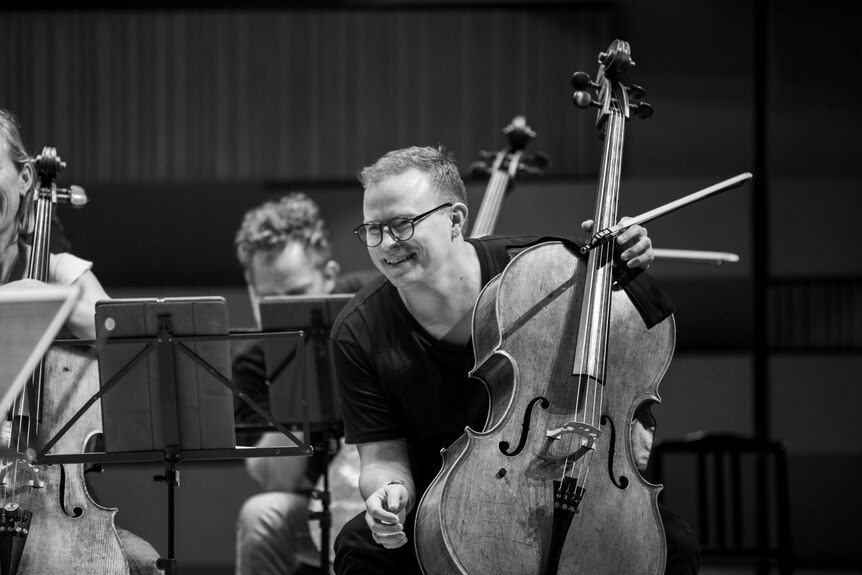 Timo-Veikko Valve is seated with his cello, laughing in rehearsal with the ACO.