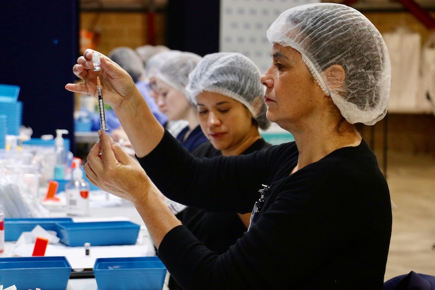 A health worker in PPE prepares a COVID vaccine in a syringe.