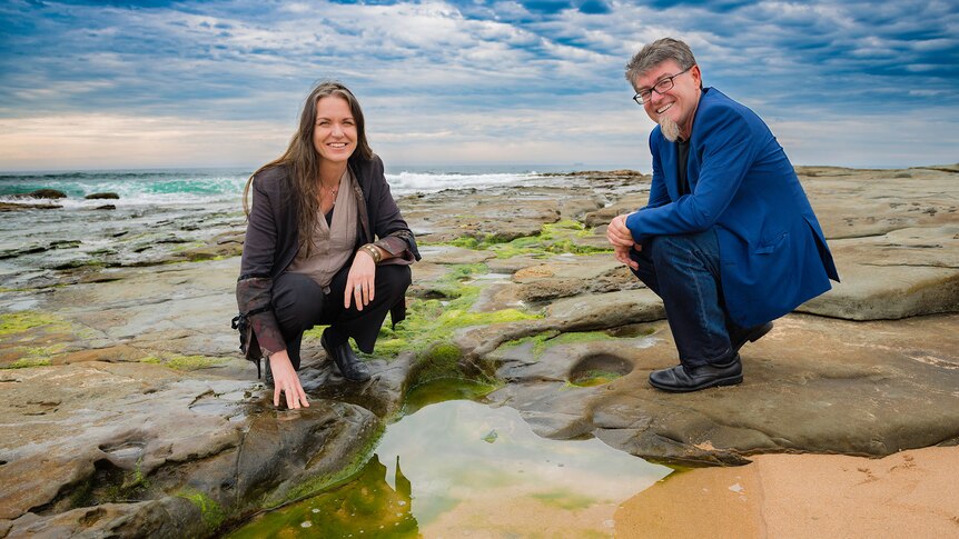 Dr Pia Winberg and Professor Gordon Wallace crouch down by the ocean.