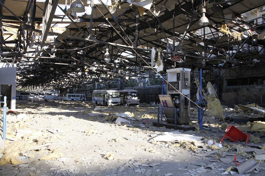 A building with exposed beams on the roof and debris all over the ground along with shattered buses.