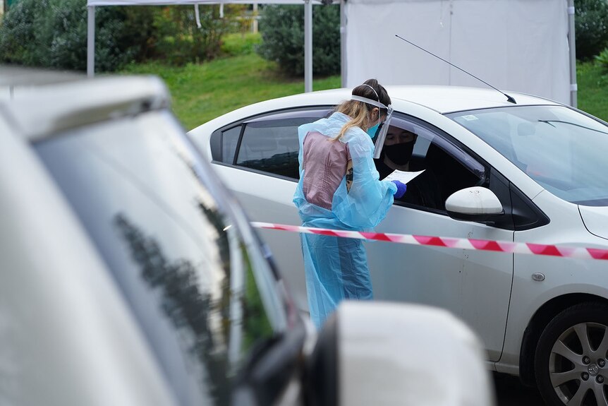 A health worker with paperwork next to a car lined up at COVID-19 testing drive-through clinic at Toowong in Brisbane